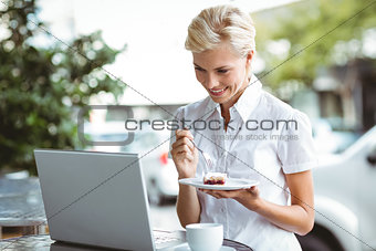 Young woman having a piece of pie using laptop