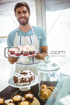 Smiling worker holding cupcakes behind the counter