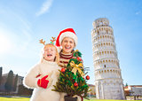 Happy woman and baby girl holding Christmas tree. Pisa, Italy