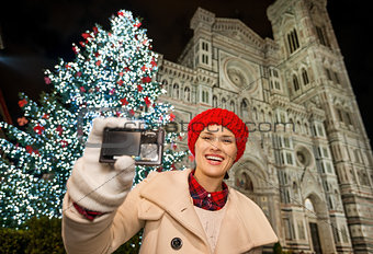 Happy woman showing photo camera near Christmas tree in Florence