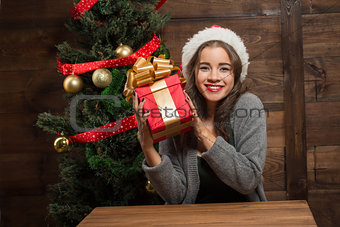 Beautiful girl sitting at the table with a present near New Year tree