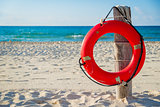 Life buoy on a pole on a sandy beach with blue ocean water