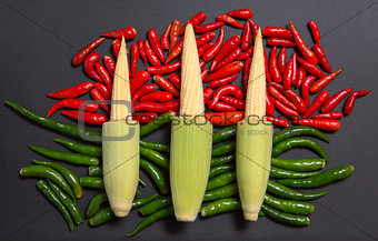 Fresh raw baby corn cobs on red and green non-stem chili peppers
