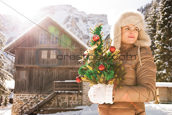 Young woman with Christmas tree standing near mountain house