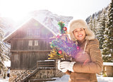 Smiling woman with Christmas tree standing near mountain house