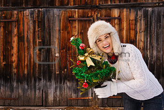 Smiling woman with Christmas tree in front of rustic wood wall