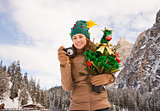 Woman with Christmas tree checking photo in front of a mountains