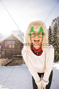 Young woman in a Christmas glasses in front of a mountain house