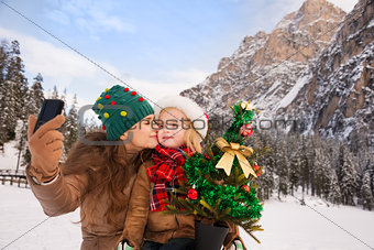 Mother and child with Christmas tree taking selfie outdoors