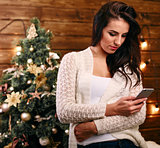 Attractive festive young woman  in front of the Xmas tree checking for Christmas messages on her mobile phone