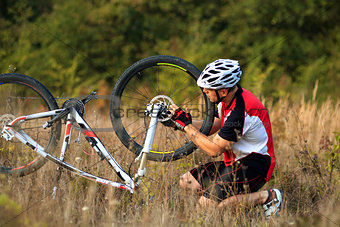 Man cyclist repairing a bike  against green nature