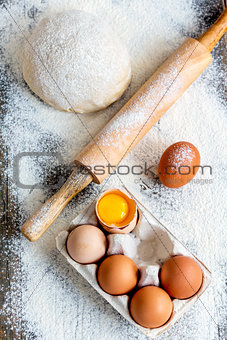 Dough, rolling pin and a tray of eggs.