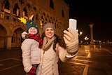 Mother with child taking selfie on Piazza San Marco in evening