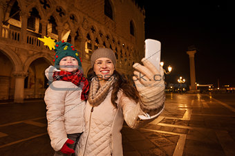 Mother with child taking selfie on Piazza San Marco in evening