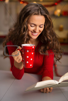 Woman with cup of chocolate and book in Christmas kitchen
