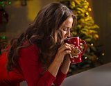 Woman having cup of hot chocolate and cookie near Christmas tree