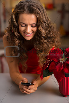 Happy young woman in red dress writing sms in Christmas kitchen