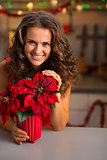 Smiling young woman with christmas rose in decorated kitchen