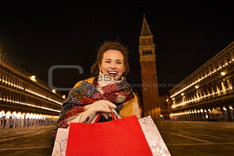 Smiling woman with shopping bags on Piazza San Marco in evening