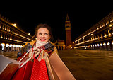 Happy woman holding shopping bags on Piazza San Marco in evening