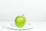 Green Apple with water drops in a plate