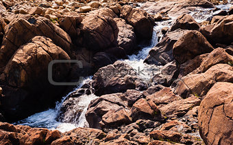 Stream flowing and splashing among bare red rocks