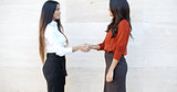 Two stylish women shaking hands outdoors