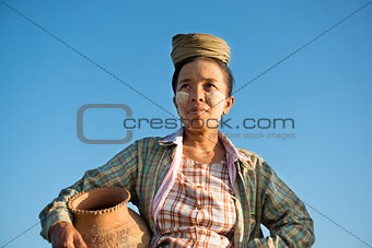 Mature Asian traditional female farmer carrying clay pot