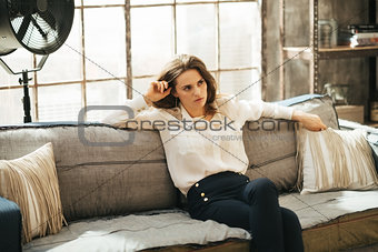 Concentrated stylish woman is sitting on couch in loft room
