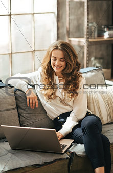 Smiling elegant woman sitting on couch and working on laptop
