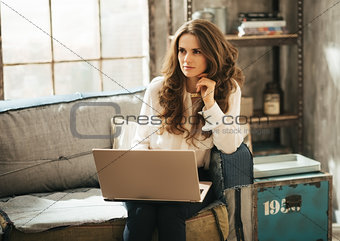 Stylish brunet woman sitting on couch and working on laptop