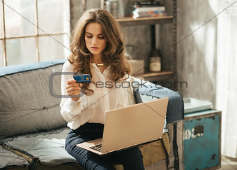 Elegant dressed woman on couch typing info from credit card