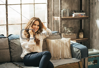 Smiling stylish woman sitting on divan and talking smartphone
