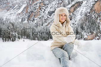 Woman in white coat and fur hat sitting on the snow outdoors