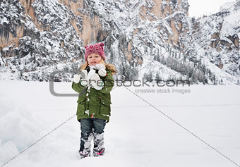 Happy child in green coat playing with snow