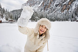 Woman in white coat and fur hat throwing snowball outdoors