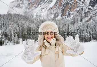 Woman in coat and fur hat showing snow-covered mittens outdoors