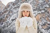 Woman in fur hat blowing snow from hands in camera outdoors
