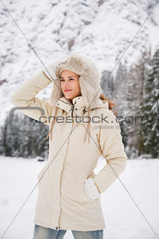 Woman in coat adjusting hat while standing in winter outdoors