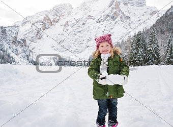 Happy child in green coat playing with snow outdoors