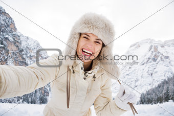 Woman in white coat and fur hat taking selfie in winter outdoors