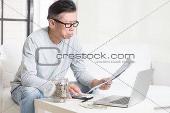 Worried mature Asian man looking at the bills.