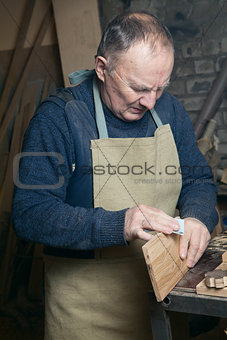 Men sandpaper grinds wood product in a workshop