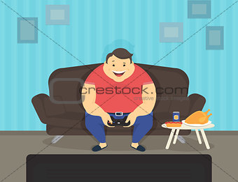 Fat man sitting at home on the sofa playing video games and eating