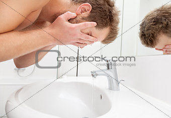 Man washing face in bathroom sink
