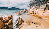 A wave crashing on rocks in a national park in Tasmania, with mountains in the background