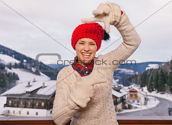 Happy woman framing with hands on balcony overlooking mountains