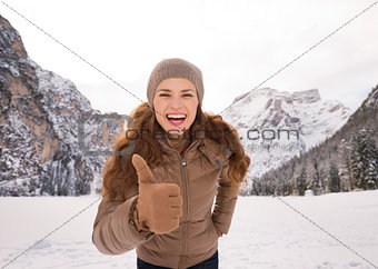Woman showing thumbs up outdoors among snow-capped mountains