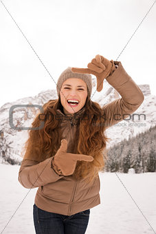 Woman framing with hands outdoors among snow-capped mountains