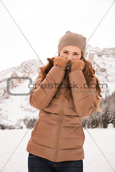 Woman hiding behind collar outdoors among snow-capped mountains
